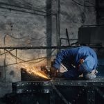 Front view of fitter in special blue uniform working with electric steel cutter machine for welding special metal. Concept of process working with grinding machine in garage.